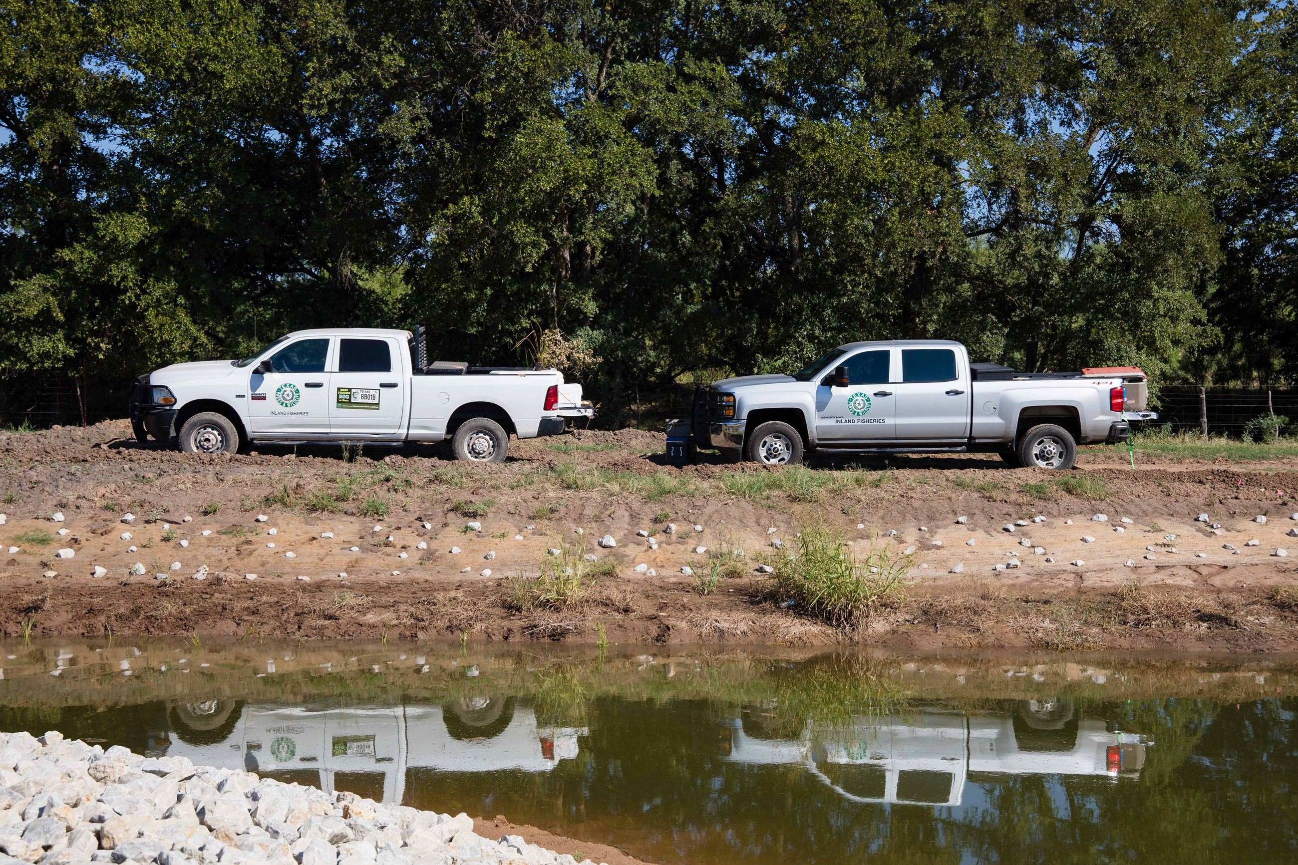 IMG of two trucks next to the water. Trees in the background.