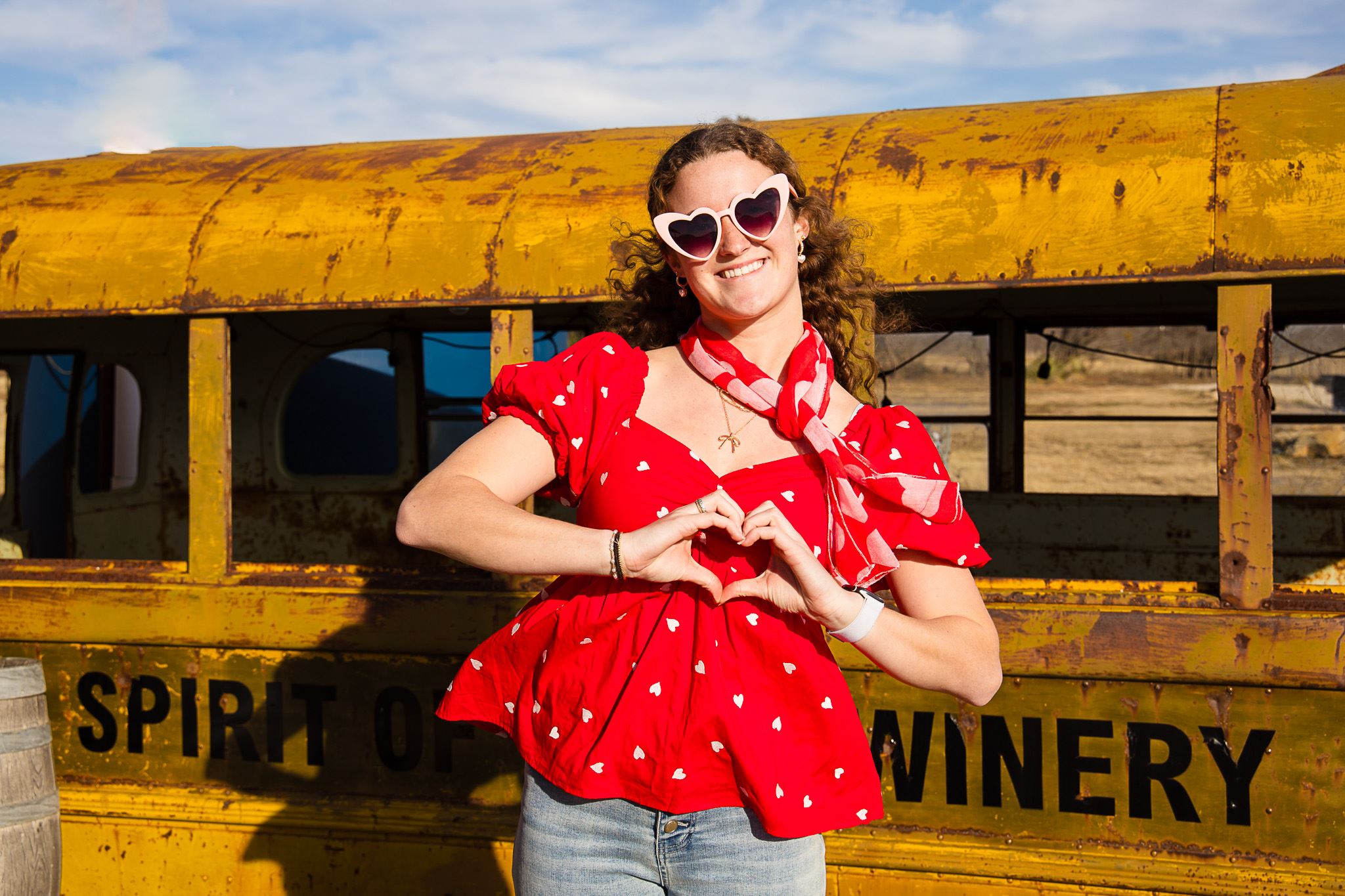 Image of a Woman Smiling & Posing a Heart with her Hands in Front of an Old School Bus