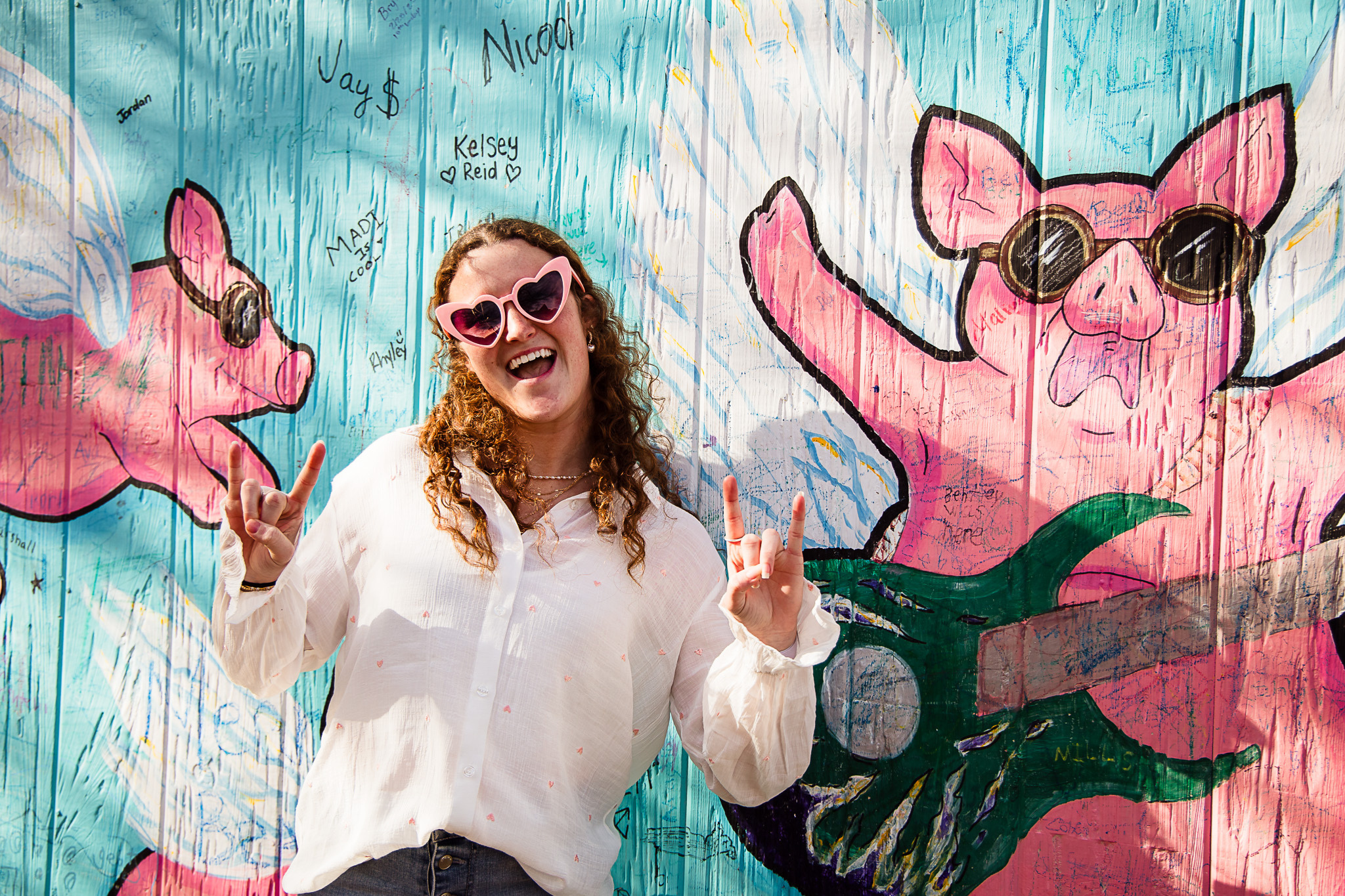 Picture in front a art mural of pigs with a guitar with a girl posing in front of it